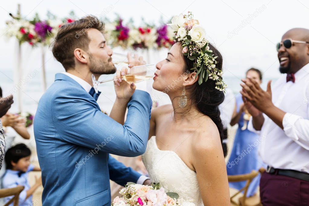Cheerful newlyweds doing love shot with champagne at beach wedding ceremony