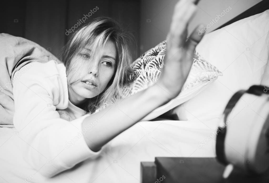 A sleepy Caucasian woman turning off the alarm