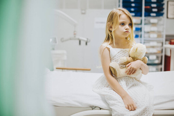 Young girl sitting alone on a hospital bed