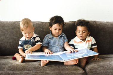 Üç küçük çocuk bir kanepede kitap okuyor