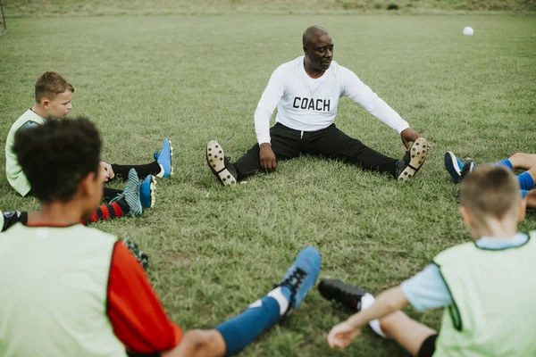 Football coach stretching with junior players