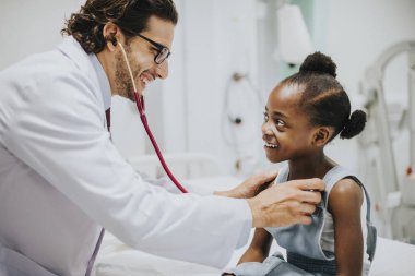 Friendly pediatrician checking a little girls heart clipart