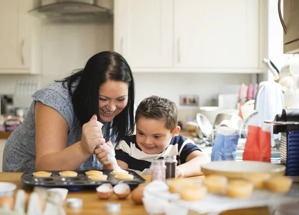 Mother helping son to put frosting onto cupcakes