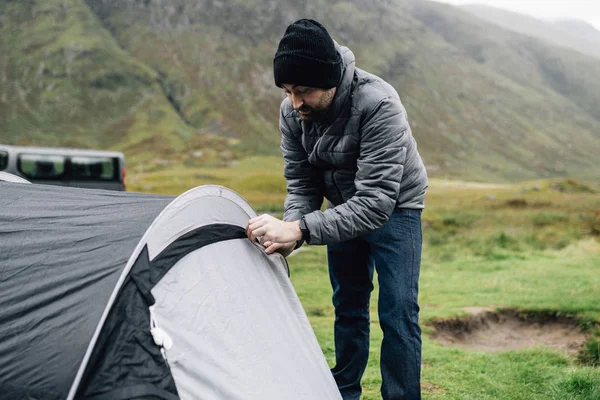 Man zipping up his tent in the raining