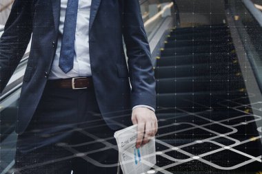 Yürüyen merdivene inen işadamı elinde gazete tutuyor