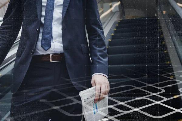 Yürüyen merdivene inen işadamı elinde gazete tutuyor