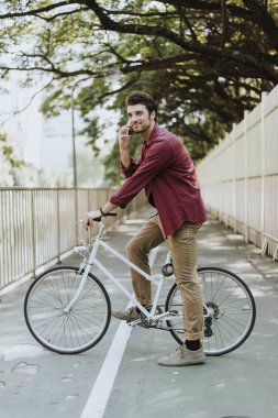 Genç beyaz adam parkta daireler çiziyor ve cep telefonu kullanıyor.