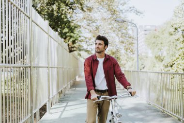 Beyaz bir adam parkta bisikletini itiyor.