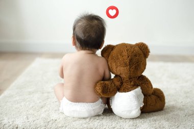 Oyuncak ayının yanında oturan bebek