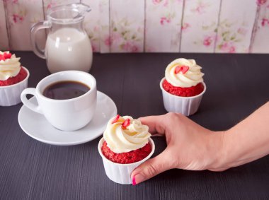 Fincan kahve ve ahşap masa kalpler ile üç cupcakes. Kadın holding cupcake.