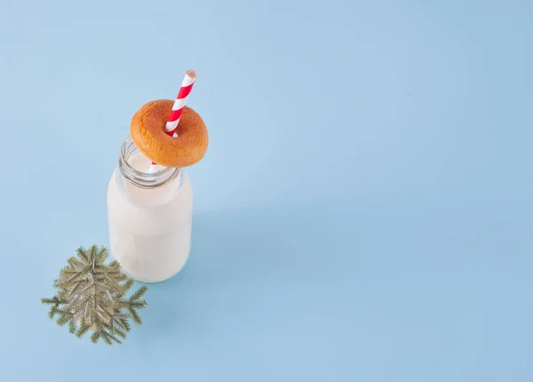 Christmas bottle with milk, donut and small Christmas tree on the blue table