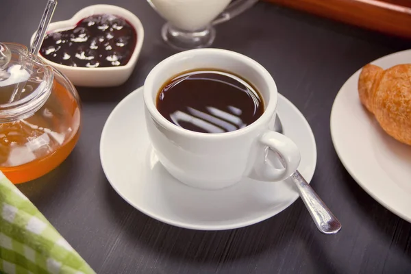 Cup of coffee with fresh croissant, honey and jam on the table. Morning breakfast.