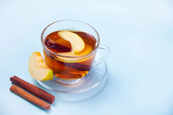 Hot drink of apple tea with cinnamon stick, star anise and clove. Seasonal apple punch in cup on the blue background.