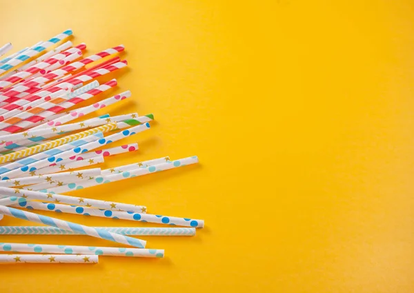 Drinking paper colorful straws for summer cocktails on yellow background. Top view.