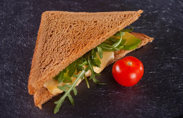 Σάντουιτς με στήθος γαλοπούλας, τυρί, μαρούλι, ρόκα, ντομάτα και κρεμμύδι σε μαύρη πλάκα — Φωτογραφία Αρχείου