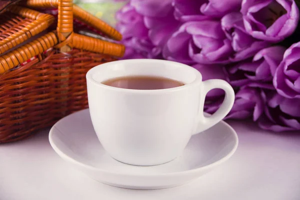 Чашка чая, корзина для пикника и фиолетовые тюльпаны на столе — стоковое фото