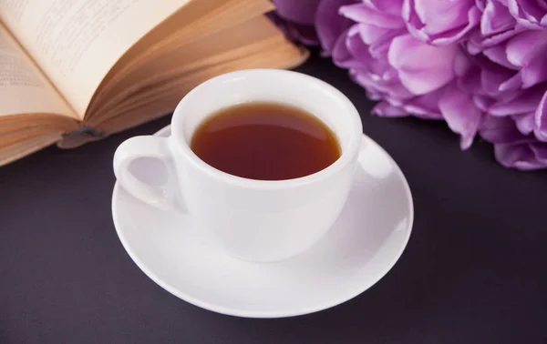 Eine Tasse Tee, Buch und violette Tulpen auf dem Tisch — Stockfoto