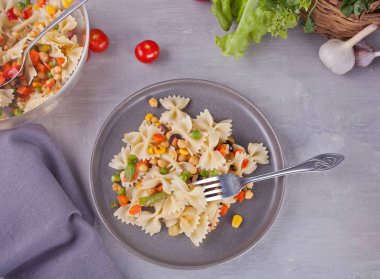 Farfalle İtalyan makarna ile gri bir arka plan üzerinde gri bir tabakta sebze karıştırın. Üstten Görünüm.