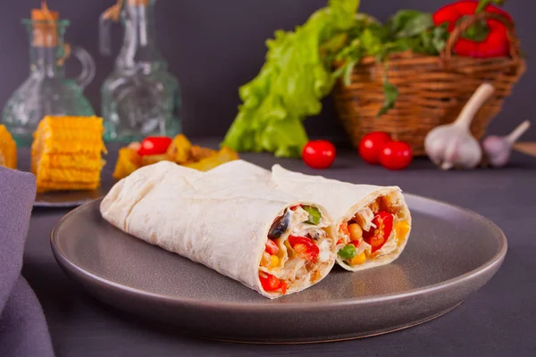 Burrito ρολά με λαχανικά στο μαύρο πίνακα και λαχανικά, ντοματίνια και σκόρδο στο παρασκήνιο — Φωτογραφία Αρχείου