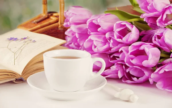 A cup of tea, book and violet tulips on the table