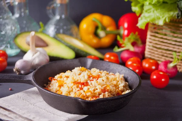 Delicious homemade vegetarian couscous with tomatoes, carrots, pepper and fresh basil on a dark kitchen table with vegetables on the background — Stock Photo, Image