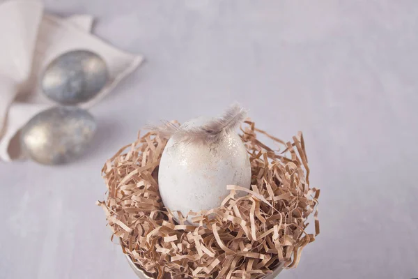 在鸟巢的复活节白蛋和两个银色蛋在灰色背景与羽毛 — 图库照片