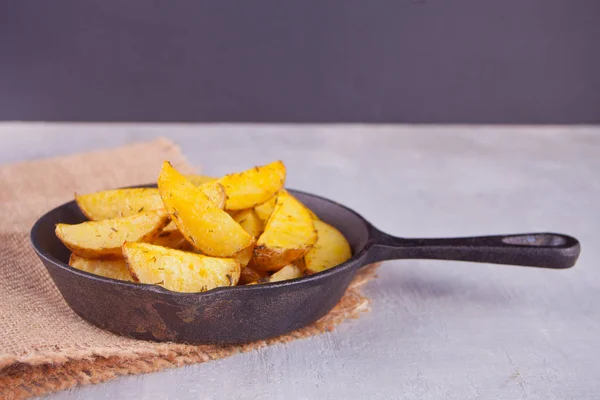 Homemade baked potato wedges with herbs on black iron pan on the gray background. — Stock Photo, Image