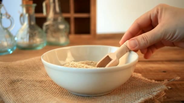 女性の手は木製の台所のテーブルのスクープでキノアの穀物を注ぐ — ストック動画