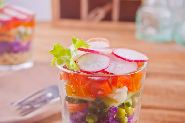 Hälsosam fräsch sallad i fullt glas med rödkål, tomat, Quinoa, grön sallad och rädisor på trä bordet — Stockfoto