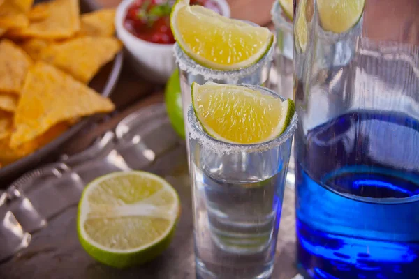 Tequila shot com limão e sal marinho e garrafa azul na bandeja — Fotografia de Stock