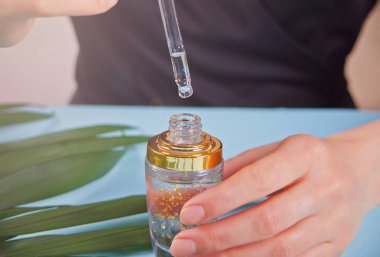 Kadının elinde altın parçacıklarının görülebildiği sıvı pipetle birlikte. Temiz bir şişede damlayan bir damla.