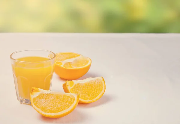 Copo de suco de laranja e fatias de frutas de laranja na mesa branca com a natureza no fundo — Fotografia de Stock