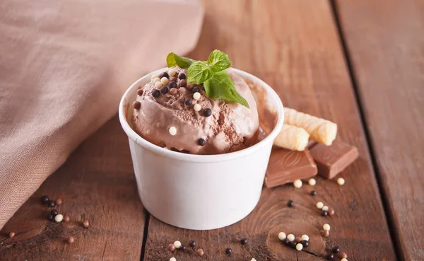 Papírová miska z čokoládové zmrzliny, vaflový kužel a lžíce pro zmrzlinu na dřevěném podkladu. — Stock fotografie