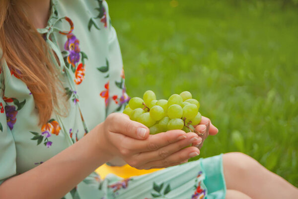 Woman sitting on the yellow cover and holding bunch of grapes.