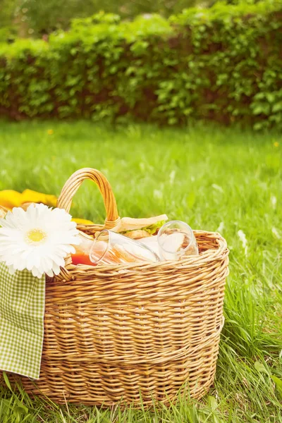 Nahaufnahme eines Picknickkorbs mit Essen, Früchten und Blumen auf dem gelben Deckel auf dem grünen Gras — Stockfoto