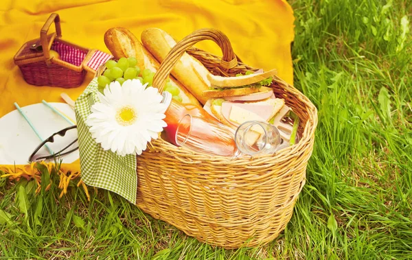 Nahaufnahme eines Picknickkorbs mit Essen, Früchten und Blumen auf dem gelben Deckel auf dem grünen Gras — Stockfoto