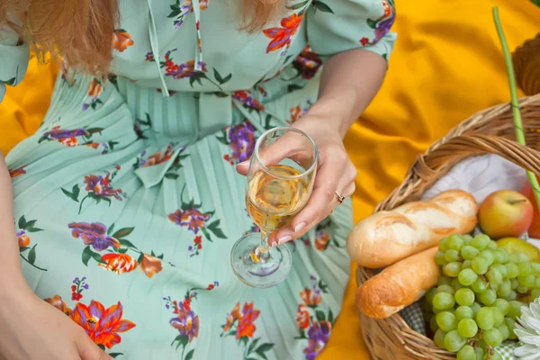 De vrouw op de picknick zit op de gele kap en houdt wijnglas vast. Vlakbij picknickmand met eten en fruit. — Stockfoto