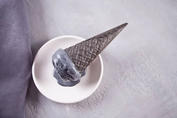 Helado negro en conos de helado con porciones tradicionales. En un plato de cerámica blanca, sobre una mesa gris con taza negra y servilleta gris . — Foto de Stock