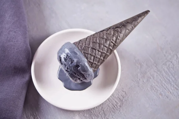 Helado negro en conos de helado con porciones tradicionales. En un plato de cerámica blanca, sobre una mesa gris con taza negra y servilleta gris . — Foto de Stock