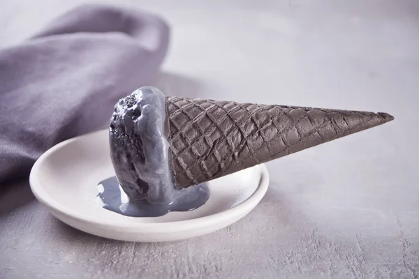 Helado negro en conos de helado con porciones tradicionales. En un plato de cerámica blanca, sobre una mesa gris con taza negra y servilleta gris . — Foto de Stock