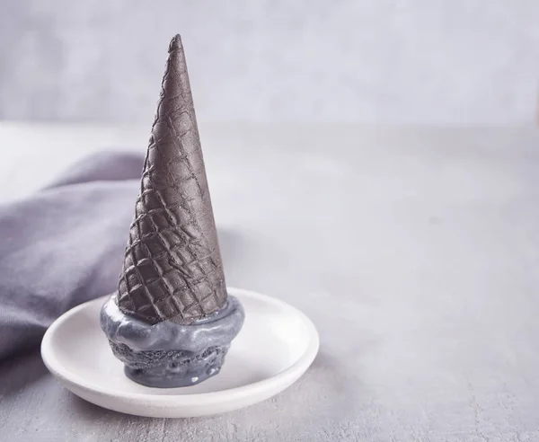 黑色冰淇淋在传统的分份冰淇淋圆锥。在白色陶瓷板上，在一张灰色的桌子上，有黑色杯子和灰色餐巾纸. — 图库照片