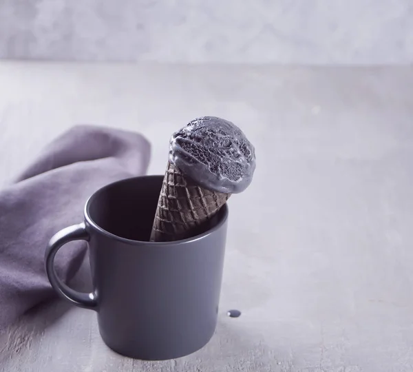 Helado negro en conos de helado con porciones tradicionales. En una taza de cerámica blanca con servilleta gris en una mesa gris — Foto de Stock