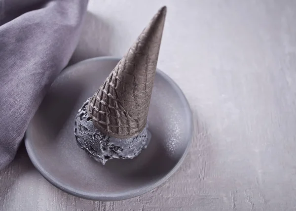 Helado negro en conos de helado con porciones tradicionales. En un plato de cerámica blanca, sobre una mesa gris con taza negra y servilleta gris . — Foto de Stock