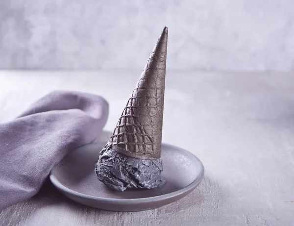 Helado negro en conos de helado con porciones tradicionales. En un plato de cerámica blanca, sobre una mesa gris con taza negra y servilleta gris . — Foto de Stock