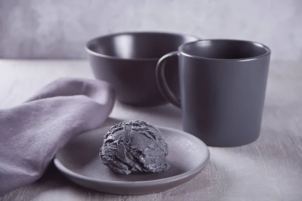 Gri bir masada gri peçete ile siyah seramik plaka üzerinde siyah dondurma — Stok fotoğraf