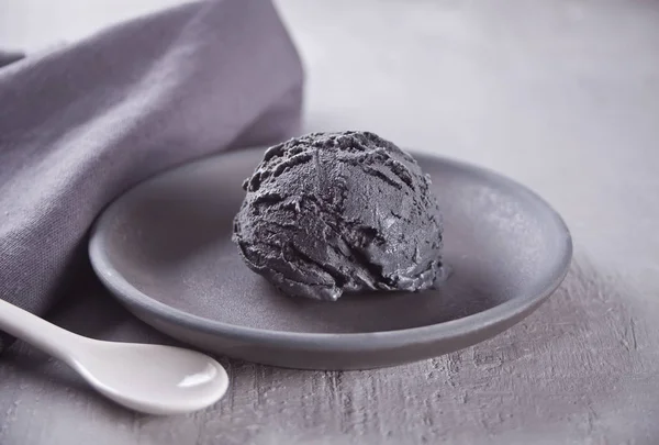 Black ice cream on a black ceramic plate with gray napkin on a gray table