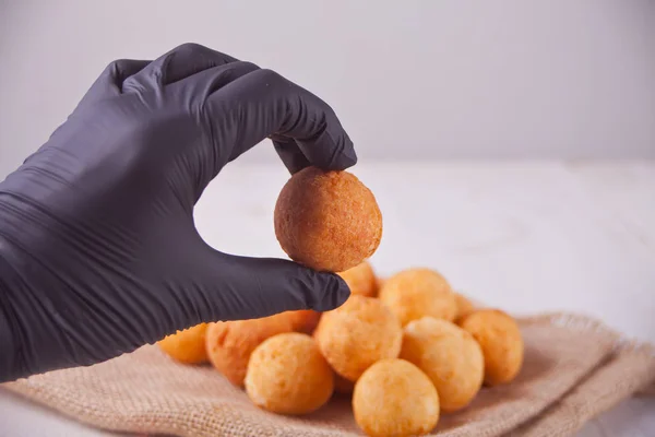 Small balls of freshly baked homemade cottage cheese doughnuts and woman's hand in black gloves holding one doughnut — Stock Photo, Image