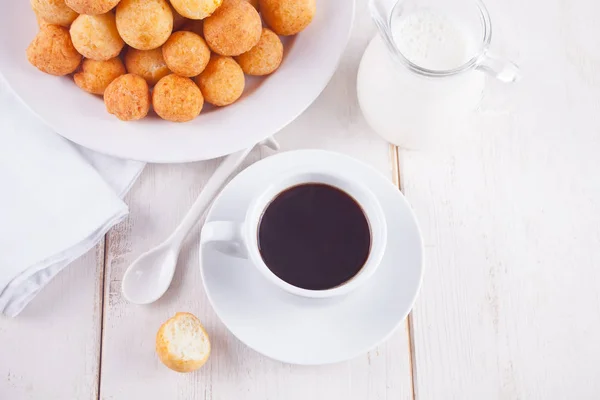Cup of coffee with small balls of freshly baked homemade cottage cheese doughnuts in a plate on a background. — Stock Photo, Image