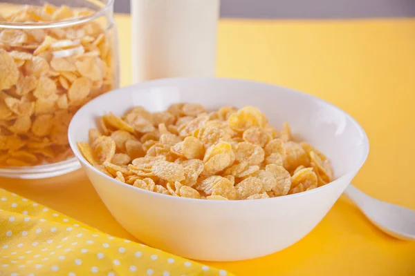 A bowl of dry corn flakes cereal on yellow background