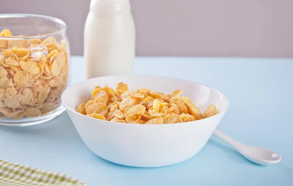 A bowl of dry corn flakes cereal on blue background